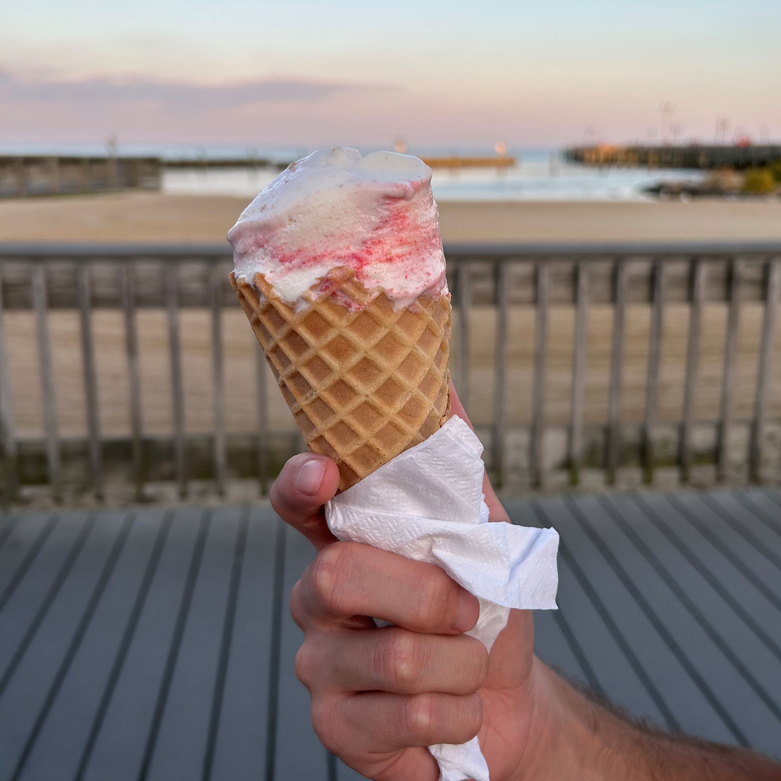 Pink ice cream on a cone in front of the boardwalk and bay 