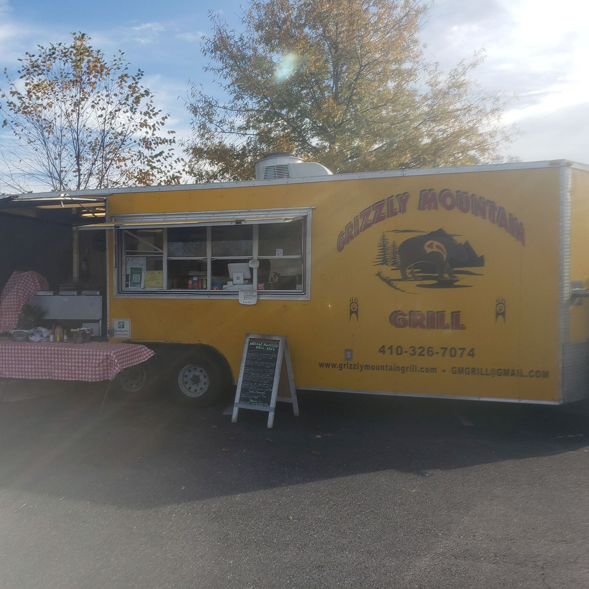 yellow food truck with grizzly mountain grill logo and an american flag and table in front